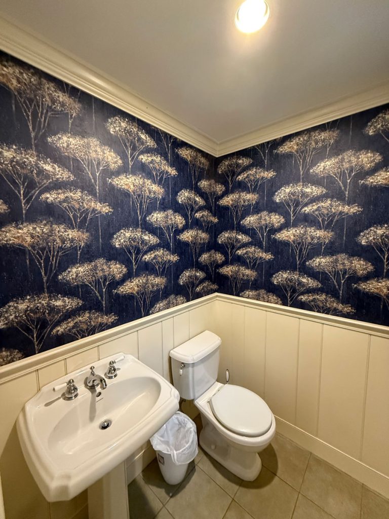 Powder room featuring dark blue floral wallpaper above white wainscoting beadboard paneling, installed