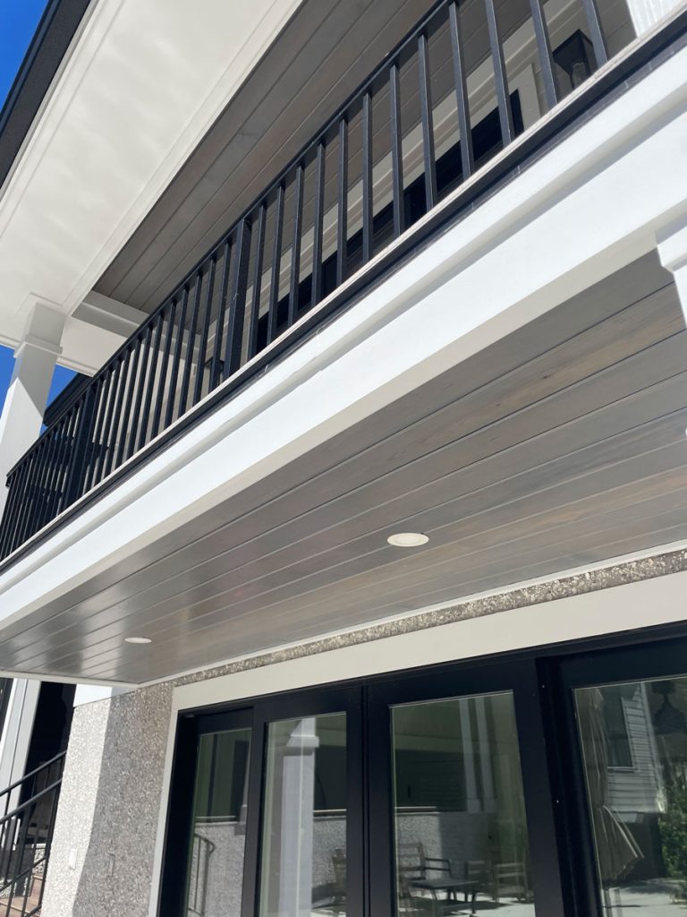 Coastal shoreline home exterior with custom grey wood soffit ceiling, white fascia trim, and black balcony railing by Simons Painting & Drywall in Connecticut.