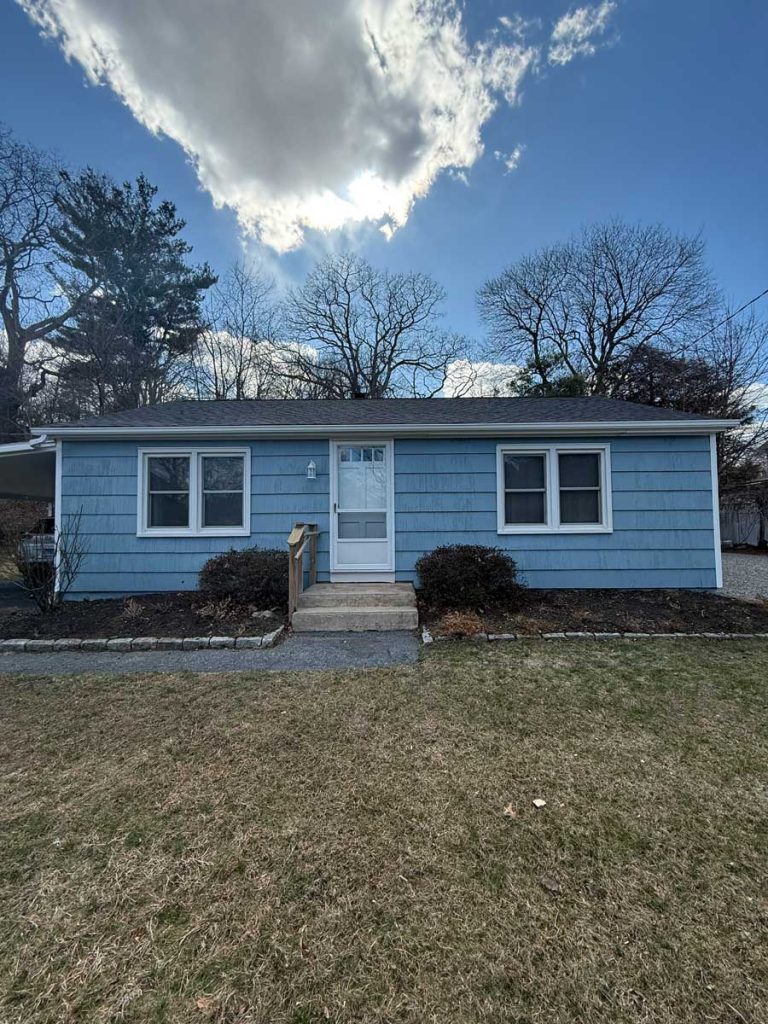 Newly painted light blue ranch-style house with crisp white trim and a front door in Connecticut, by Simons Painting & Drywall.