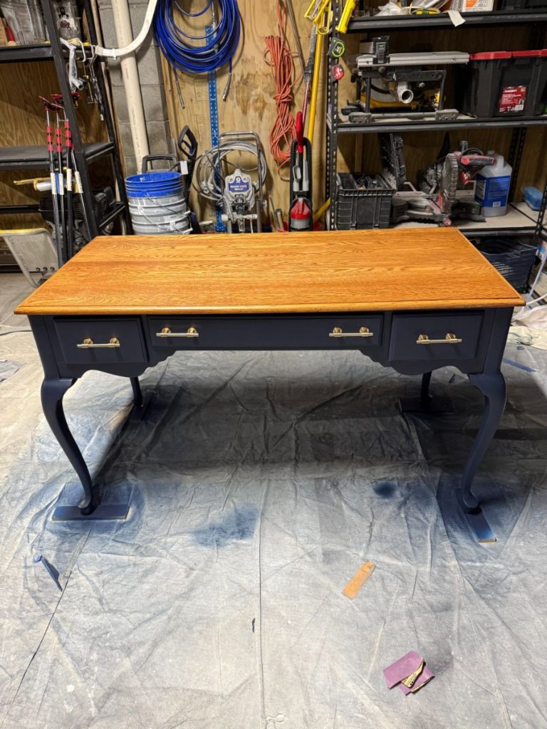 Refinished vintage desk with a newly stained wood top and dark navy painted base during the spray-finishing process, by Simons Painting & Drywall in CT.