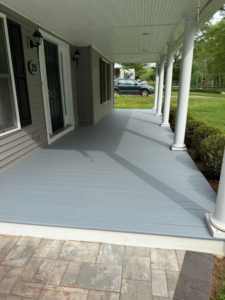 A freshly painted light gray covered front porch deck on a house in Connecticut, with white support columns, white trim, and gray siding, completed by Simons Painting & Drywall.