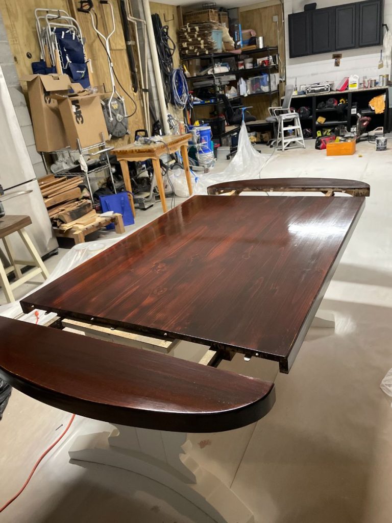 Refinished dining table with a high-gloss dark stain and clearcoat finish in the workshop.